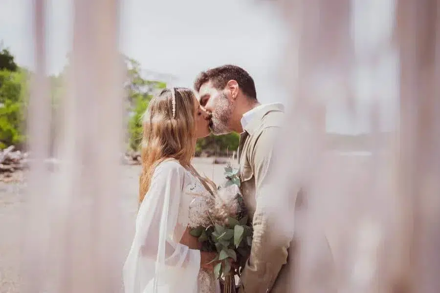 wedding ceremony photography costa rica-21 | Pacific Photography Couple kissing outdoors at a wedding, woman in a white dress holding a greenery bouquet.