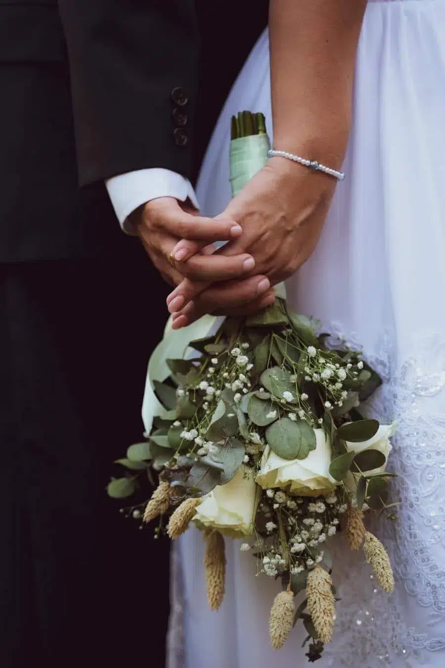 Close-up of a bride and groom holding a bouquet of white roses and greenery.