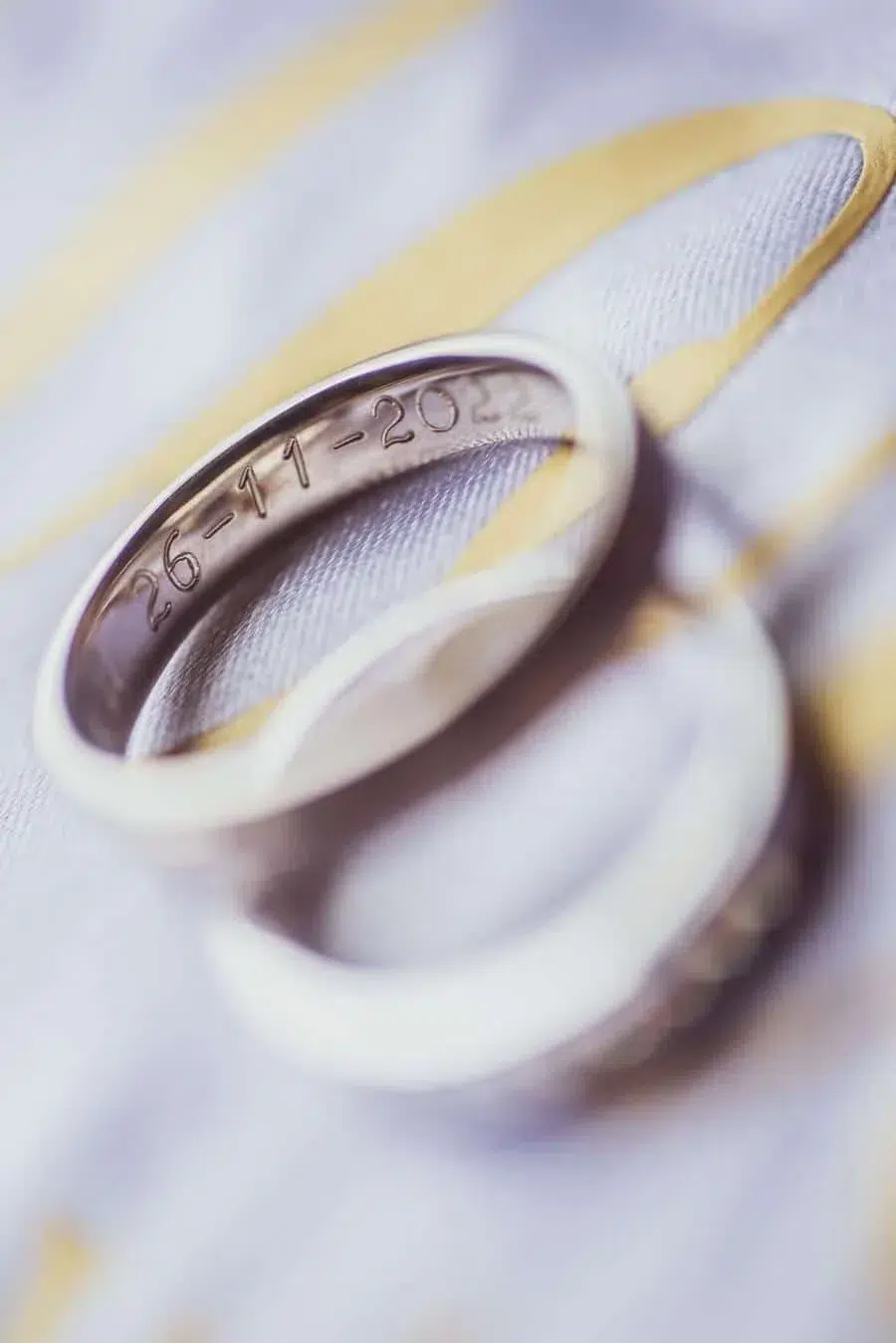 Close-up of a silver wedding ring with engraved date 26-11-2021 resting on patterned fabric.